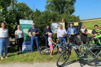An einem Waldrand steht eine Gruppe von Menschen vor Plakatwänden
