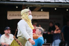 Eine junge Frau in Mittelalterlicher Verkleidung passiert einen gut besuchten Marktstand. 