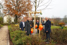 Sechs Männer stehen um einen frischgepflanzten Baum herum und gießen ihn. 