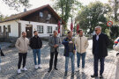 Eine Gruppe Menschen steht vor einem Dorfladen, ein Mann erklärt.