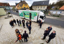 Eine Gruppe von Menschen steht vor dem Mobilen Dorfladen, das Bild ist aus der Vogelperspektive aufgenommen.