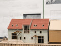 Ein Hausmodell ist in Nahaufnahme zu sehen, es hat drei Stockwerke, eine grünliche Fassade und ein rotes Dach sowie große Fenster.