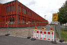 Ein Gebäude ist mit einem Bauzaun eingezäunt. Auch der Geh- und Radweg daneben ist gesperrt und wird mit einem Schild umgeleitet. 