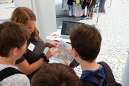 Eine Frau und drei Jungen schauen sich gemeinsam eine Karte mit bunteingezeichneten Flurstücken an.
