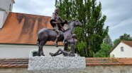 Das Bild zeigt die Bronzeskulptur des heiligen St. Martin, die auf dem Kirchplatz in Wallnsdorf steht.