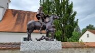 Das Bild zeigt die Bronzeskulptur des heiligen St. Martin, die auf dem Kirchplatz in Wallnsdorf steht.