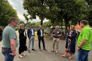 Sieben Personen stehen im Halbkreis, einer von ihnen spricht zu den anderen. 