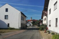 Eine Straße, die an Häusern vorbei durch einen Ort führt.