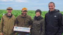 Eine Menschengruppe steht vor einem Feld und hält ein Schild mit dem boden:ständig-Logo in den Händen.