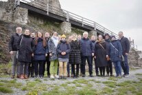 Eine Gruppe von Männern und Frauen steht vor einer Burgmauer.