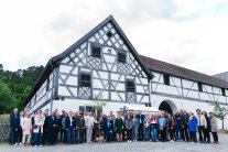 Eine große Gruppe von Menschen steht vor einem alten Bauernhof. 
