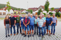 Zwei Frauen und neun Männer stehen auf einem gepflasterten Gehweg an einer Straße. 