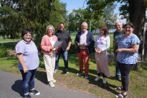 Eine Gruppe von Menschen steht im Halbkreis im Freien und blickt in die Kamera.