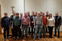 14 Personen stehen vor einer weißen Wand für ein Gruppenfoto zusammen.