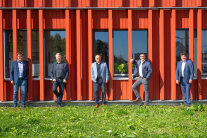 Fünf Männer stehen vor der Holzfassade eines modernen Gebäudes.