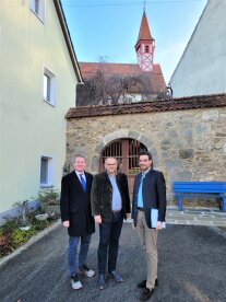 Drei Männer stehen vor einer historischen Wand. 