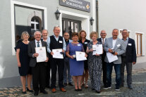 Ein großes Gruppenbild mit elf Personen, fünf von ihnen halten Urkunden in den Händen. 
