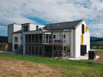 Das Bild zeigt das Gebäude von außen, von der Hinterseite. Man sieht zwei Balkone und eine Fensterfront. 