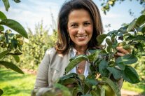 Lachende Staatsministerin Michaela Kaniber hinter einem Ast eines Streuobstbaums. 