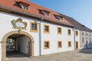 Die Fassade eines zweistöckigen Klosters erhält ockergelbe Fensterumrahmingen und eine weiße Fassade.