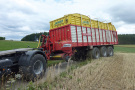 Zugmaschine und beladener Wagen fahren vom Acker auf den angrenzenden zu schmalen Weg.