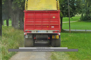 Landwirtschaftlicher Anhänger, von dem ein Rad auf dem Bankett läuft. Unter den Reifen Schemamontage eines Hauptwirtschaftsweges mit einer Fahrbahnbreite von 3,5 Metern plus links und rechts jeweils 0,75 Meter befahrbarer Unterbau.